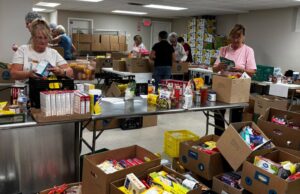 Stettler & District Food Bank Drive Raises Over $10K In Donations Volunteers sorting and packing canned goods and boxed foods at a busy food pantry workstation.