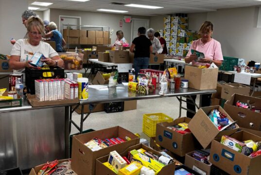 Stettler & District Food Bank Drive Raises Over $10K In Donations Volunteers sorting and packing canned goods and boxed foods at a busy food pantry workstation.