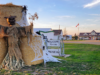 Stettler Booseum 2026: Haunted House Opens At The Museum Courthouse A straw scarecrow figure on a large hay bale with tattered cloth, near a 'Welcome to the Museum' sign and decorative white web, in a rural town during sunset.