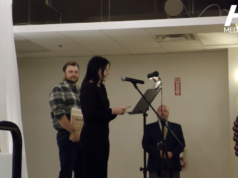 Stettler Awards Gala Celebrates Local Citizens & Businesses Woman speaks at a microphone at a podium on a stage; a man in plaid stands with award plaques behind her, festive balloons to the right.