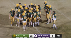 Stettler Wildcats Win First Home Game Since 2022 Football players in green and gold huddle on a dusty field as a scoreboard shows Stettler 22, Iron Ridge 8 in the 4th quarter (Stettler, Alberta, Canada). -Informative image conveying team celebration and score.