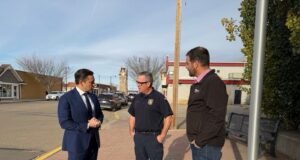 Pierre Poilievre: The Best Of Canada Answered The Call In Wainwright Three men stand on a brick sidewalk in a small‑town street, conversing: a man in a navy suit, a police officer, and a casually dressed man.